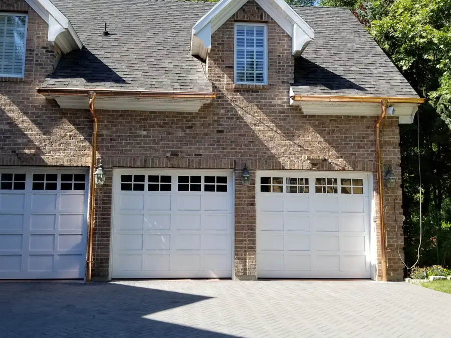 Brick home with copper gutters and downspouts over white garage doors