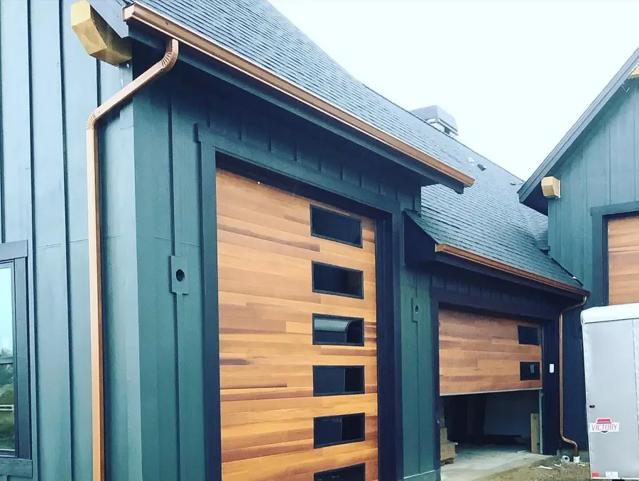 Green board-and-batten home with copper gutter and downspout beside a cedar garage door